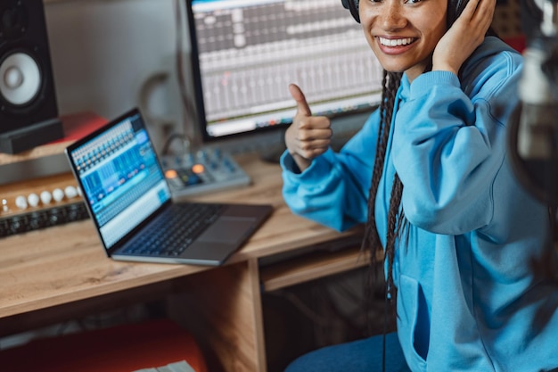 Closeup of pretty african anchorwoman with headphones showing thumb up while broadcasting on radio