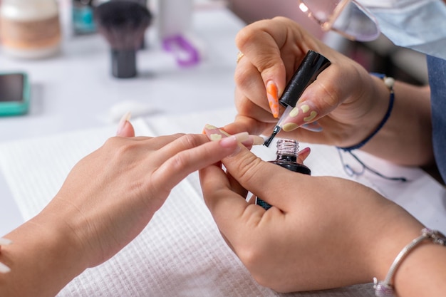 Closeup of a professional manicurist's hands applying a clear base coat to her client