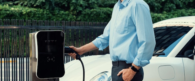 Closeup progressive businessman plugs charger plug from charging station to EV