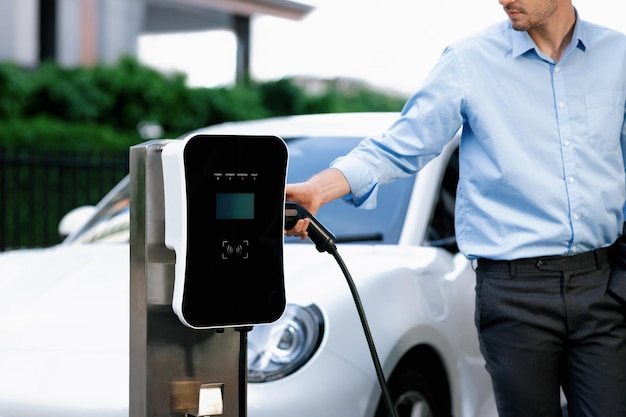 Closeup progressive businessman plugs charger plug from charging station to EV