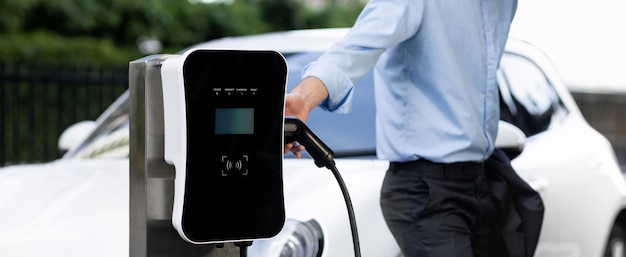 Closeup progressive businessman with electric vehicle at charging station