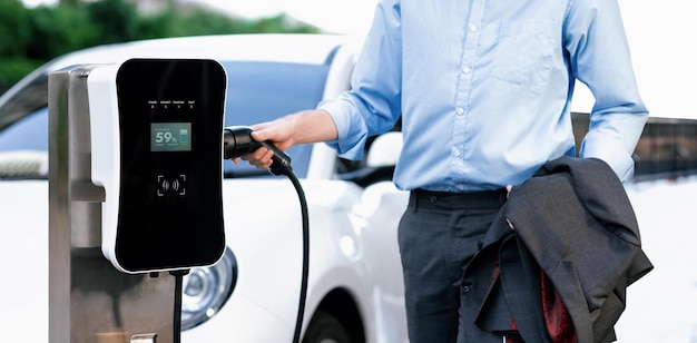 Closeup progressive businessman with electric vehicle at charging station