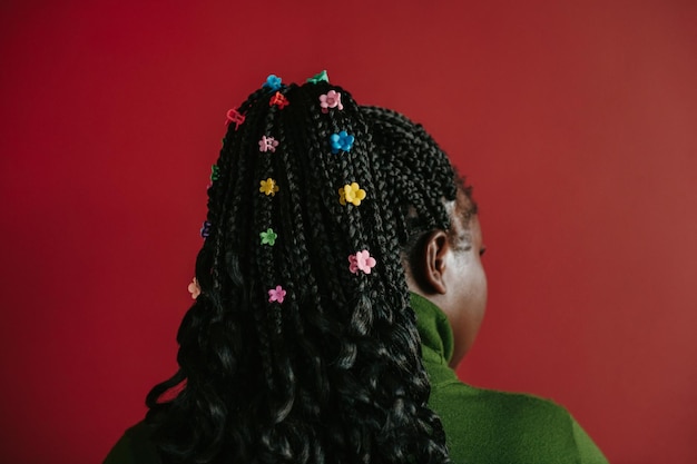 Closeup rear view of African woman with braided hair and colorful clips standing on red background