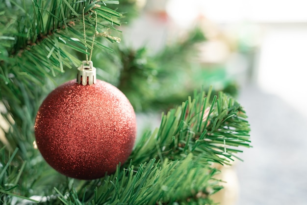 Closeup of red ball hanging from a decorated Christmas tree with copy space. Christmas and New year holidays background.