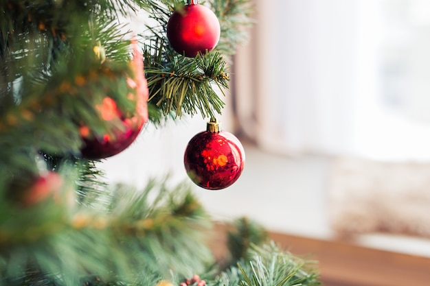 Closeup of red baubles hanging from a decorated Christmas tree.