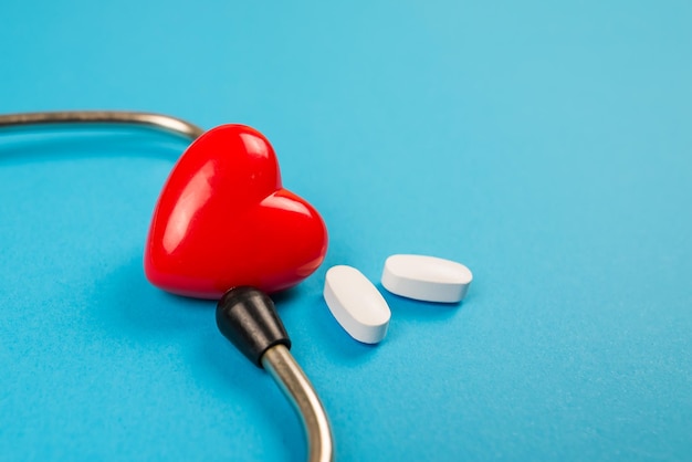 Closeup of a red heart with a stethoscope and pills on a blue background Medical concept