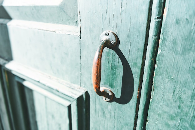 Closeup of a red paint handle on an old green door.