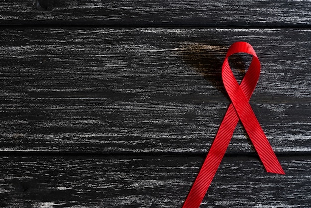 Photo closeup red ribbon awareness on black wooden table background  for world aids day campaign