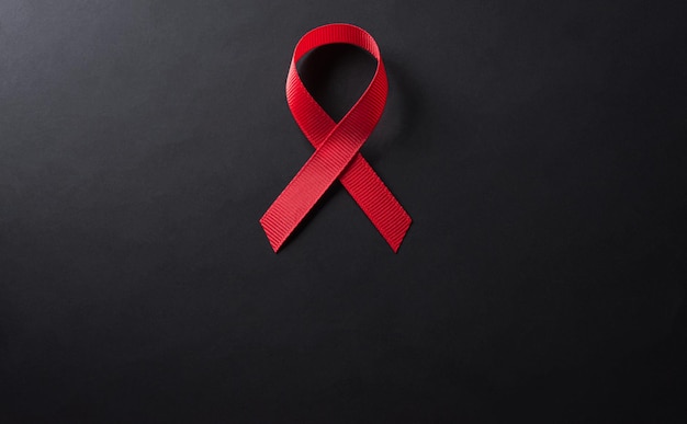 Closeup red ribbon HIV world AIDS day awareness ribbon on black background Healthcare and medicine concept