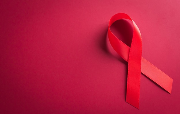 Closeup red ribbon HIV world AIDS day awareness ribbon on red background Healthcare and medicine concept