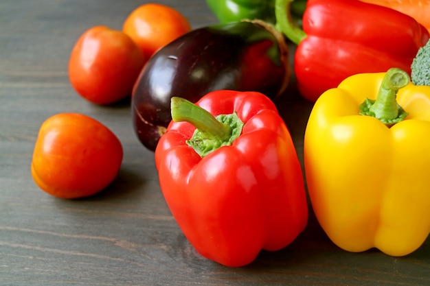 Closeup of red and yellow bell peppers with another colorful fresh vegetables on a wooden table