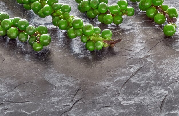 Closeup on resh green peppercorns on gray slate stone, space