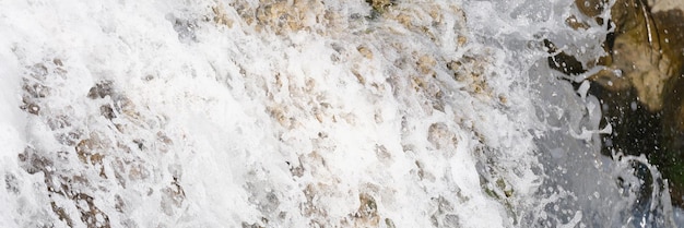 Closeup of river waterfall stream flows over mossy stones bubbling water of cascade with white