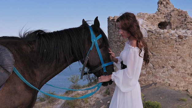 Closeup A romantic girl caressing her horse against the backdrop of a mountainsea landscape The concept of riding Authentic video Slow Motion 4K video