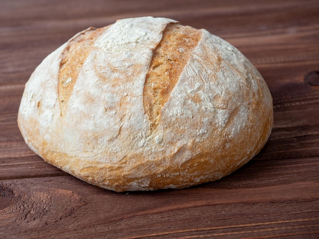 Closeup of a round loaf of wheat bread lying on a brown wooden background Baking bakery concept Side view