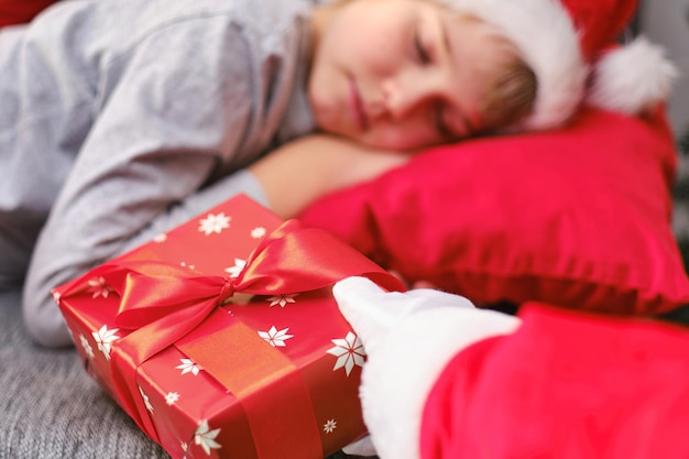 Closeup Santa's hand lays a Christmas gift to a sleeping child