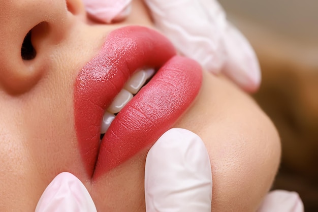 Closeup of sexy lips of young models on which permanent lip makeup is performed the master stretches the tips of the model's lips with his fingers