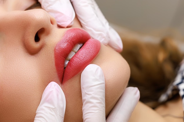 Closeup of sexy lips of young models on which permanent lip makeup is performed the master stretches the tips of the model's lips with his fingers