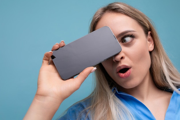 Closeup of a shocked european blonde girl holding a smartphone screen with a mockup for an