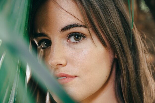 Closeup shot of an attractive brunette girl with a perfect skin near the green plant