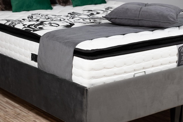 Closeup shot of a bed with gray fabric upholstery, mattress, blanket and cushions