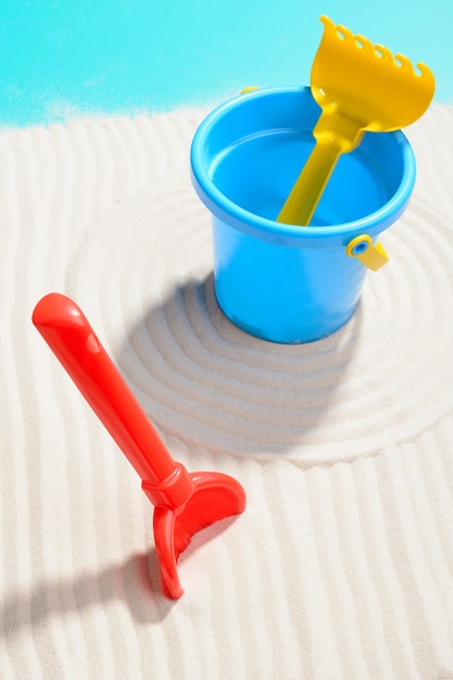 Closeup shot of blue bucket with shovel and rake on sand