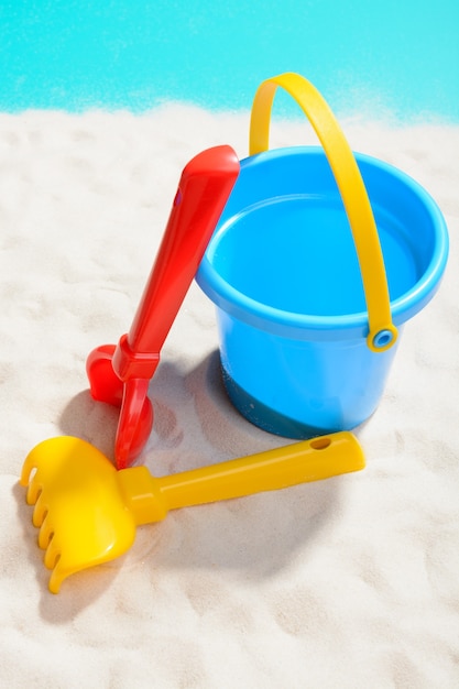 Closeup shot of blue bucket with shovel and rake on sand