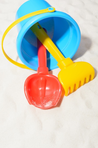 Closeup shot of blue bucket with shovel and rake on sand