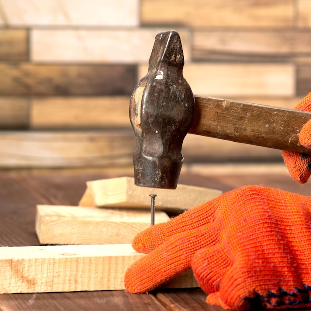 Closeup shot of a carpenter in orange work gloves hammers a nail into a wooden board