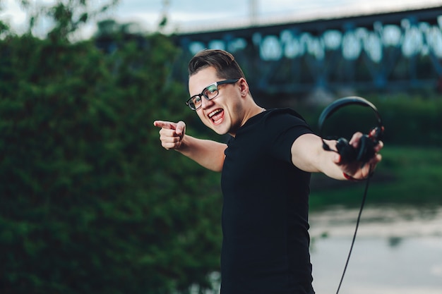 Closeup shot of casual young man in hipster glasses with headphones on the summer nature background