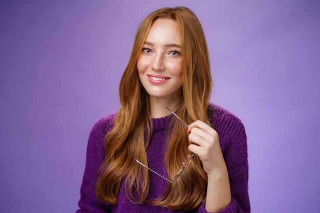 Closeup shot of charming tender and cute redhead woman in purple sweater holding glasses and smiling...