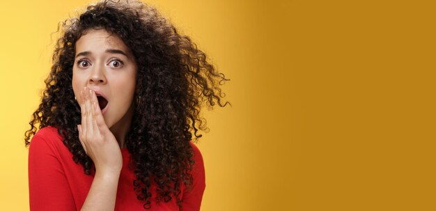 Closeup shot of concerned and shocked worried woman with curly hairstyle open mouth wide and coverin