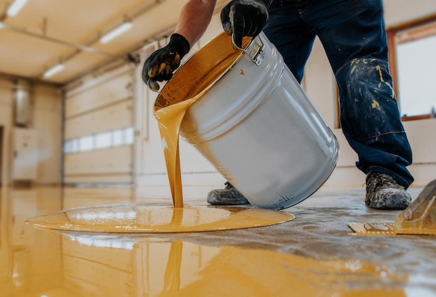 Closeup shot of a construction worker pouring out epoxy resin from a bucket onto a floor