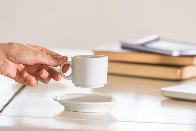 Closeup shot delicate hand lifting a white coffee cup a laptop computer