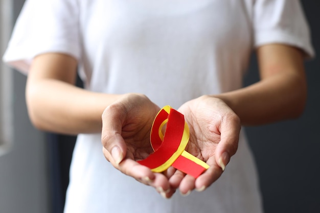 Closeup shot of female hands holding red yellow ribbon to support patient with hepatic disease Hep