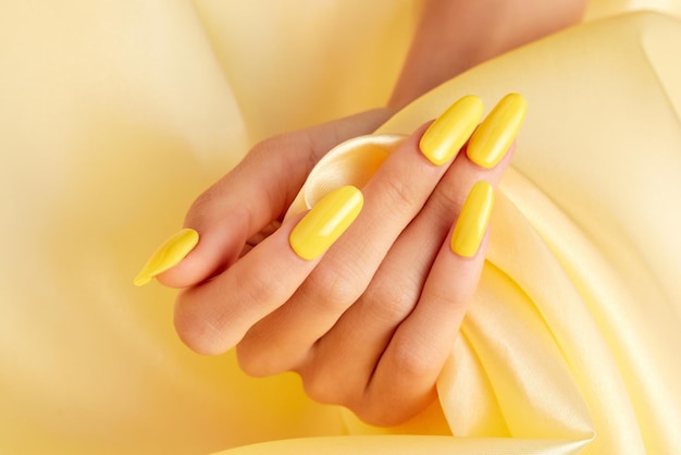 Closeup shot of a female's hand with yellow nail polish on a yellow silk fabric