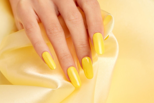 Closeup shot of a female's hand with yellow nail polish on a yellow silk fabric