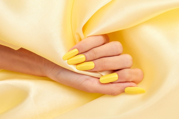 Closeup shot of a female's hand with yellow nail polish on a yellow silk fabric