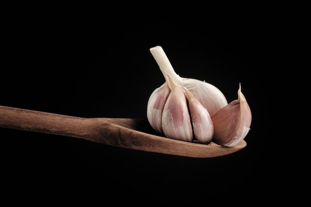 Closeup shot of the garlic head in a wooden spoon isolated on a black surface