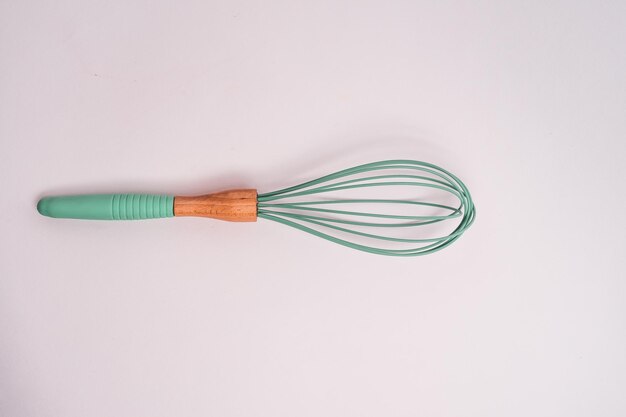 Closeup shot of a green kitchen whisk isolated on a light-colored background