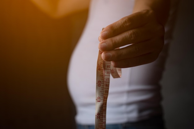 Closeup shot of hand catch the measure tape with white shirt orange light planning exercise and loss weight for good health in the feature healthcare and gym concept copy space for text or design