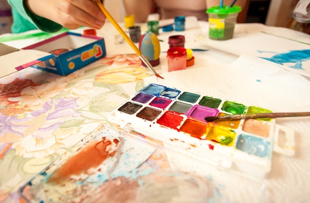 Closeup shot of little girl holding brush and taking watercolor