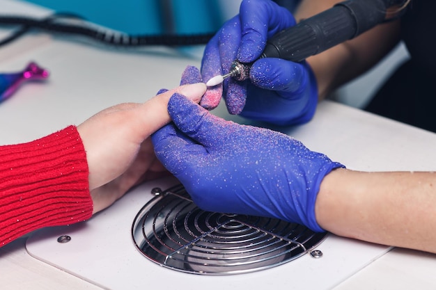 Closeup shot of a master drill removes old nail polish from nails during a manicure in a salon