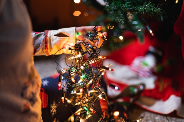 Closeup shot of a person in cozy pajamas holding illuminated Christmas lights