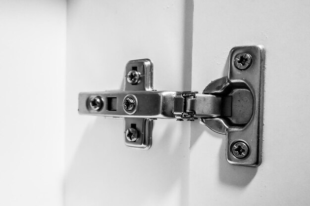 Photo closeup shot of silver furniture hinges with a closer in a white shelf