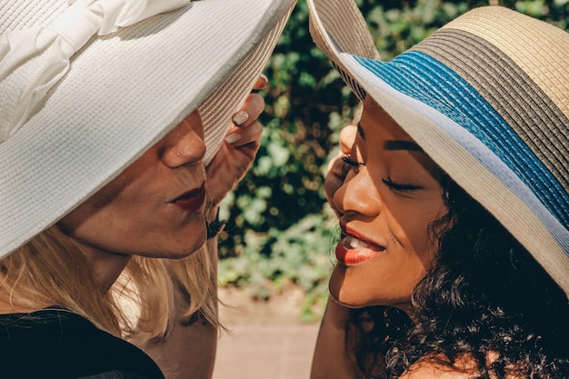 Closeup shot of two attractive women with summer hats posing happily under the sun