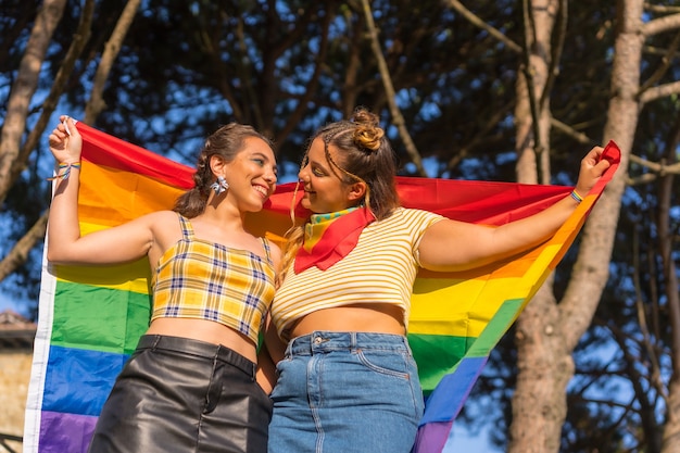 A closeup shot of two young Caucasian females holding LGBT pride flag outdoors