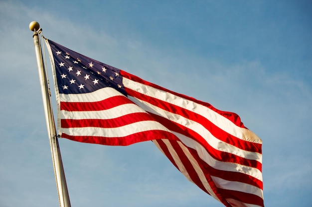 Closeup shot of the waving American flag against a blue cloudy sky on a sunny day