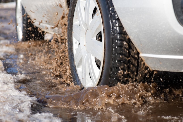 Closeup shot of a wheel of a car in dirty puddle Countryside road in bad condition in Spring