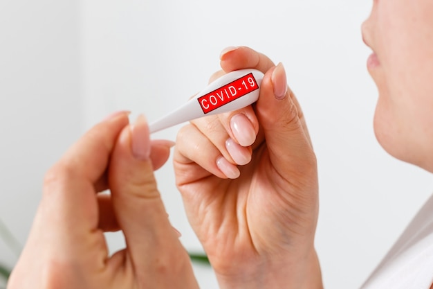 Closeup shot of a woman looking at thermometer. Female hands holding a digital thermometer. Girl measures the temperature. Shallow depth of field with focus on thermometer.